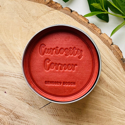 Rusty Red Sensory dough container with 'Curiosity Corner' branding on a wooden surface.